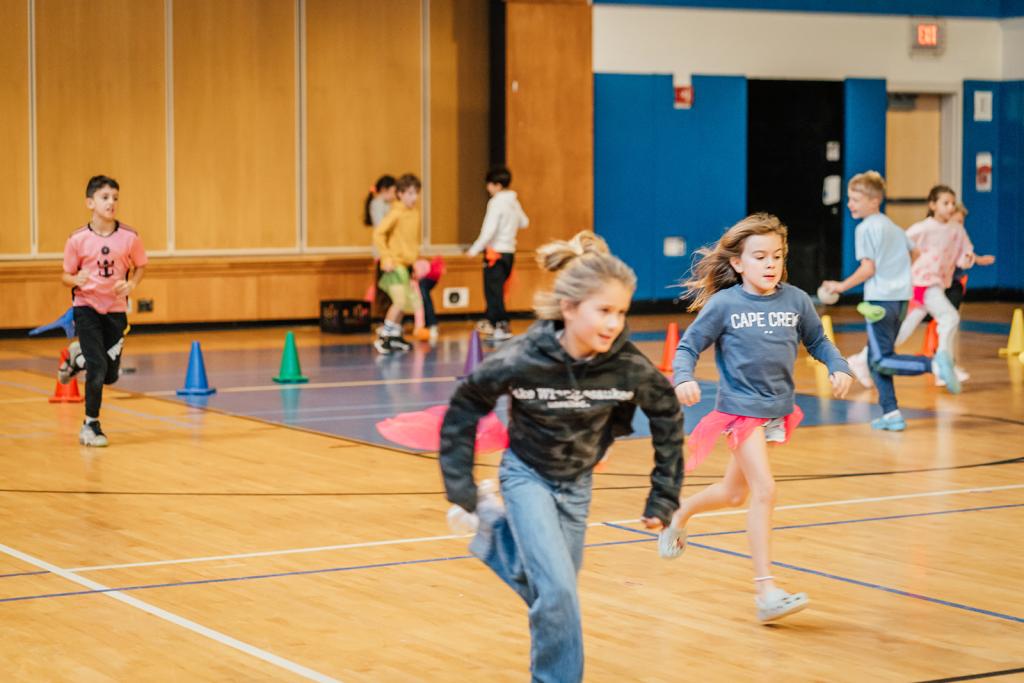 Children run and play in a brightly lit gymnasium during a physical activity.