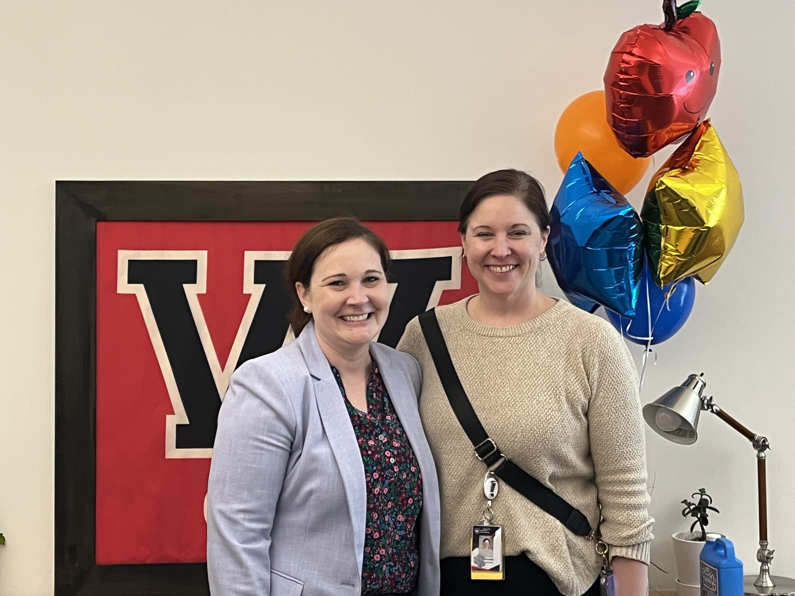Two women smile, posing together in front of a large 'W' logo.