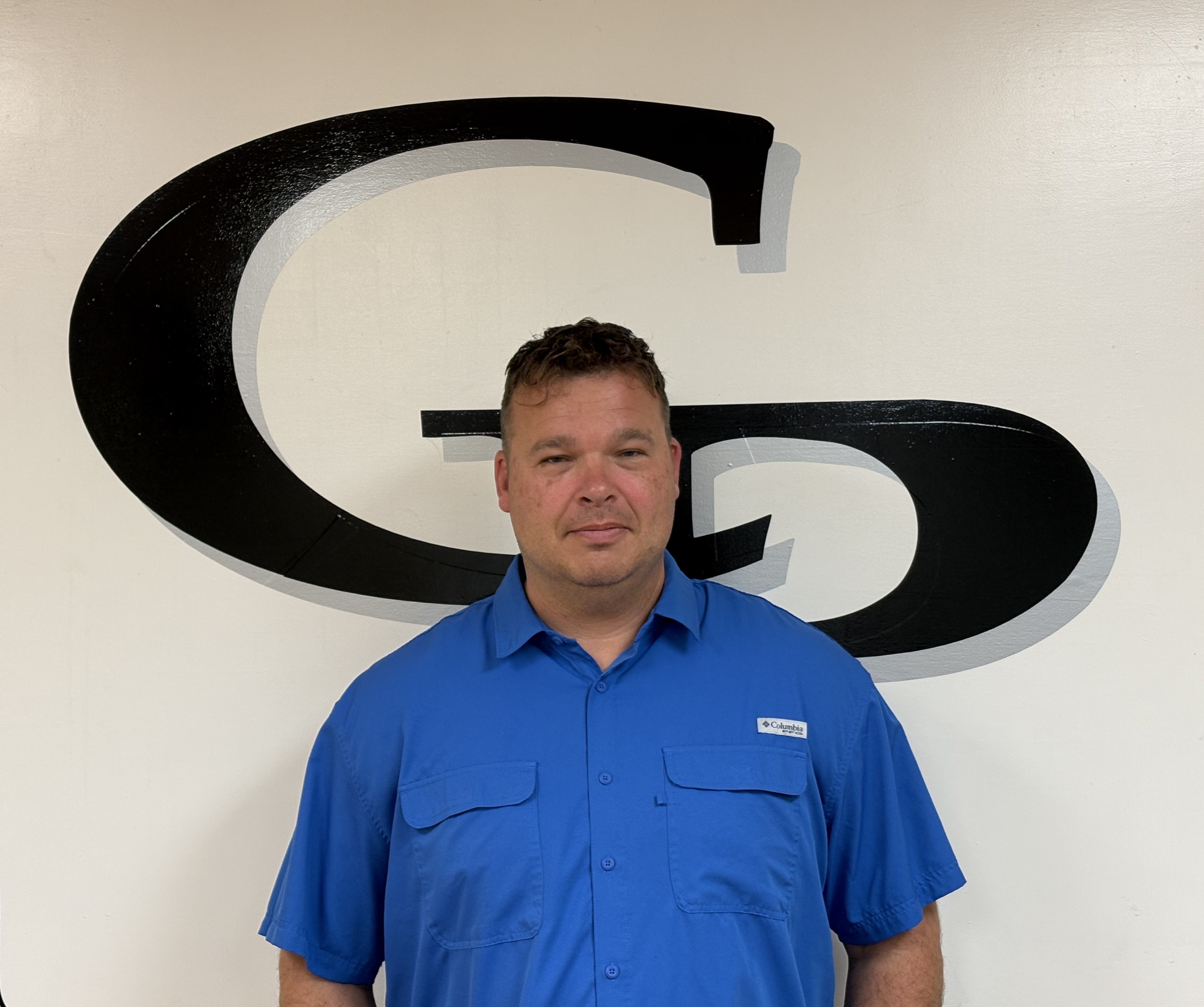A man in a blue shirt smiles in front of a large 'G' logo.