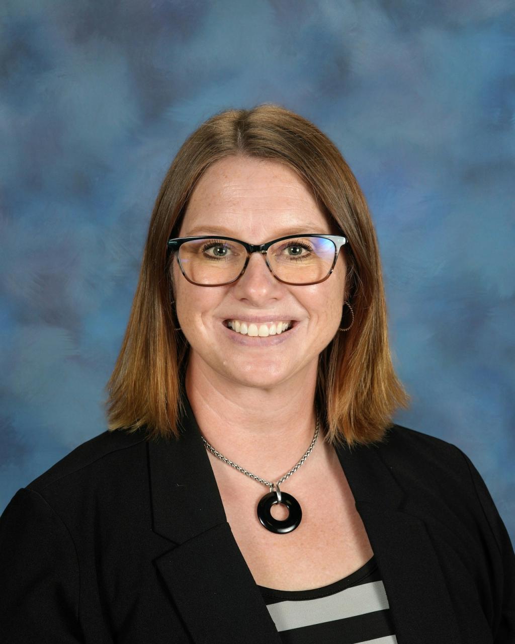 A woman with glasses smiles at the camera, wearing a black blazer.