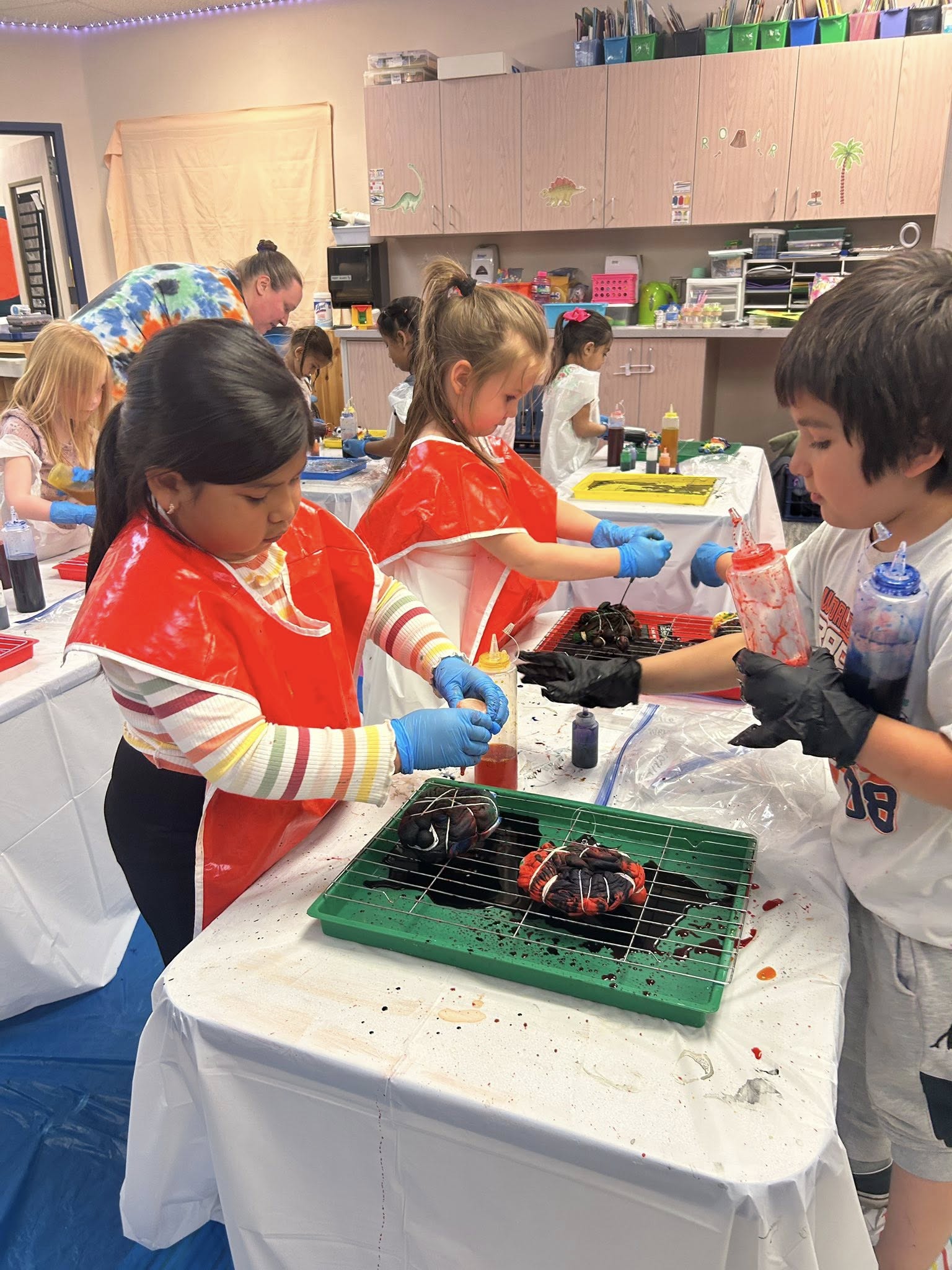 Children in aprons and gloves engage in a creative art project at a table.