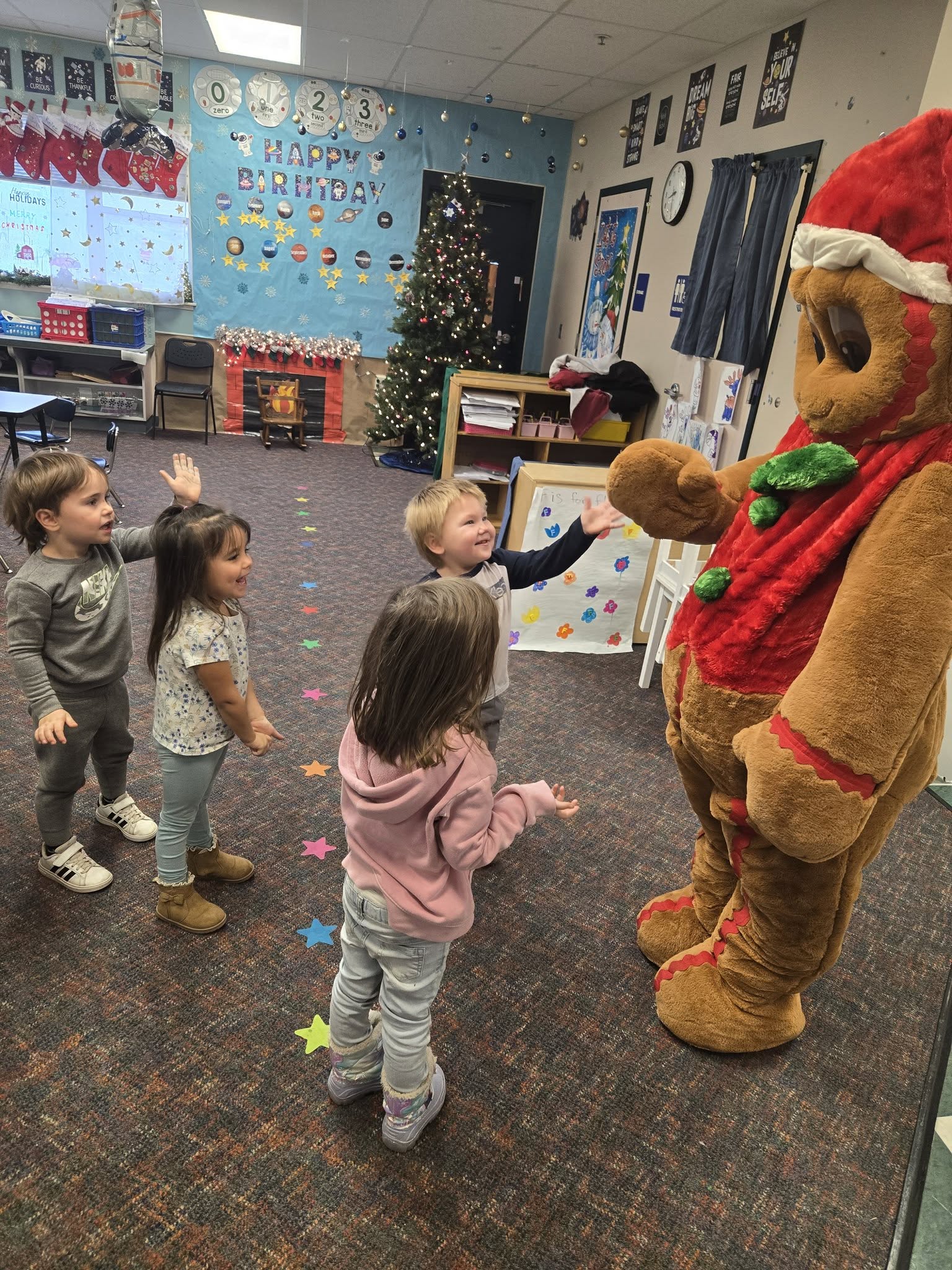 Children interact with a gingerbread man character in a decorated room.