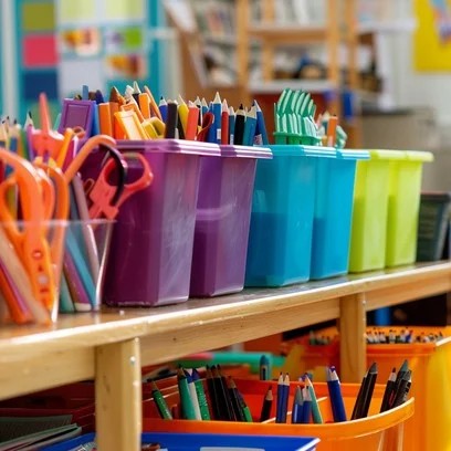 Colorful art supplies like scissors, markers, and crayons are neatly organized in bins on a wooden shelf.