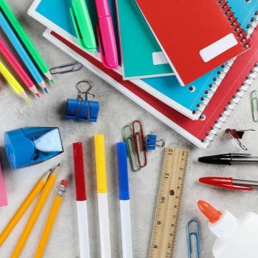 A colorful assortment of school supplies, including notebooks, pens, pencils, and a ruler, are laid out on a light gray surface.