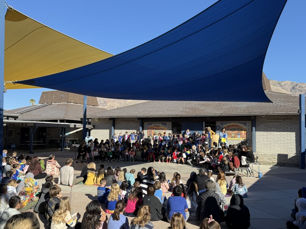 Students and adults gather outdoors under shade structures for an event.