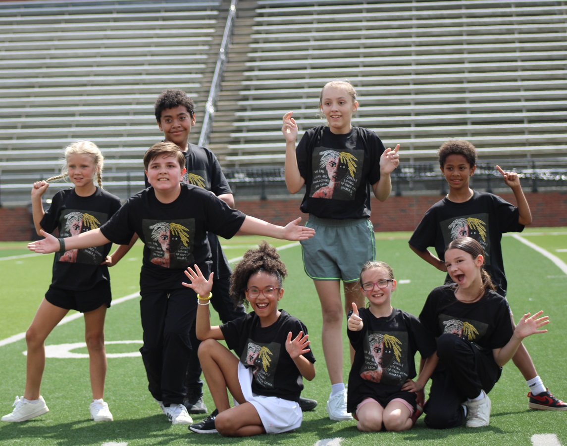 A group of children in matching black t-shirts pose on a green field.