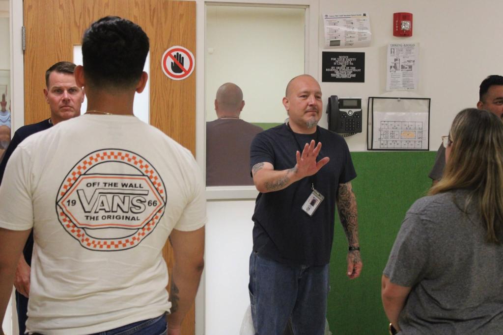 A man in a dark t-shirt gestures with his hand while speaking to a group of people.