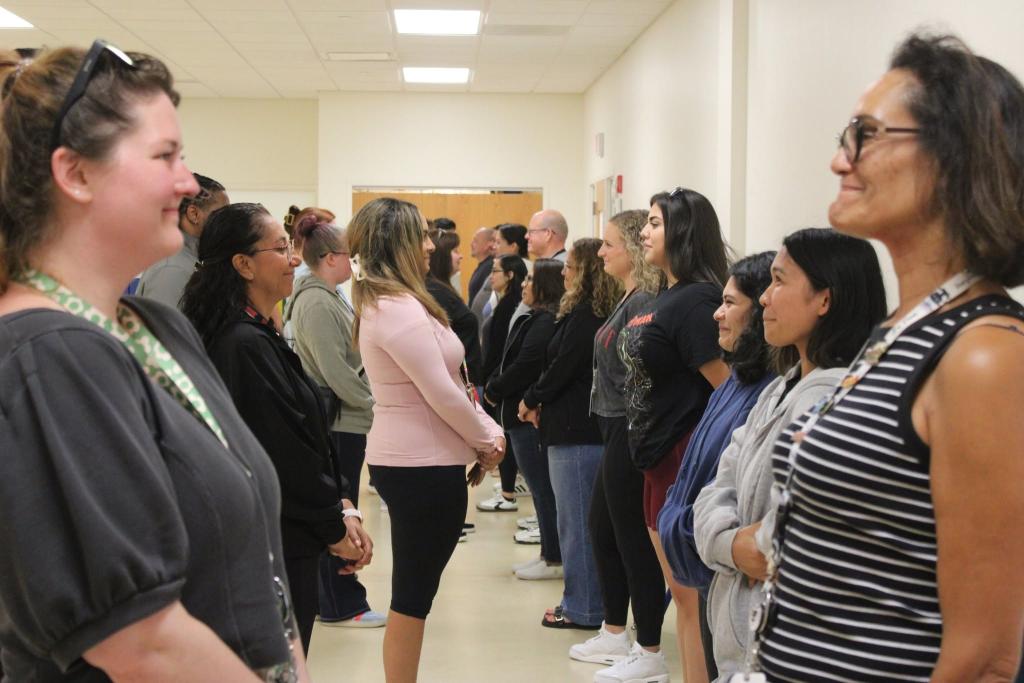 A diverse group of people stand in a line, facing forward in a well-lit indoor space.