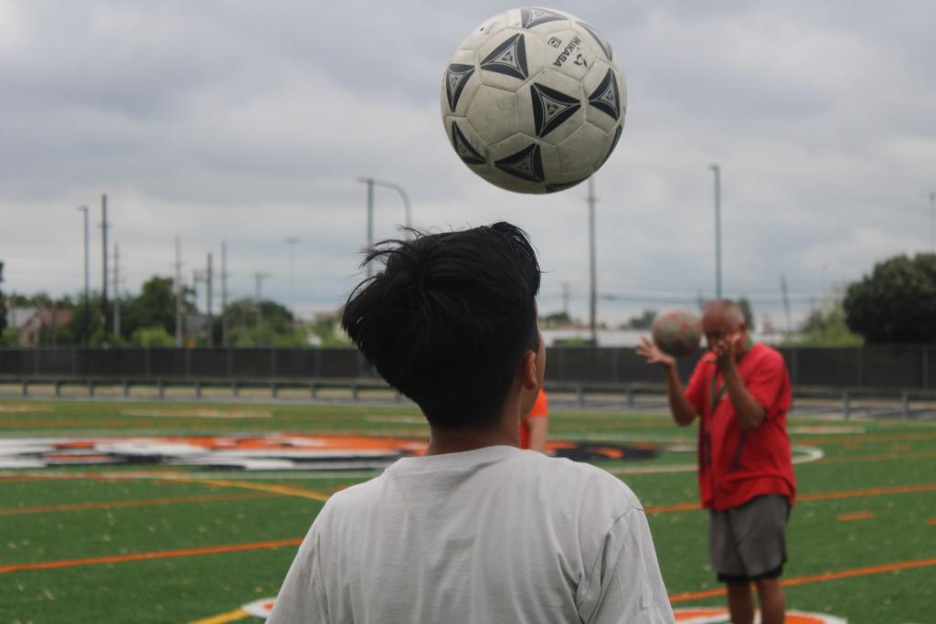 Two people play soccer on a green field, one about to head the ball.