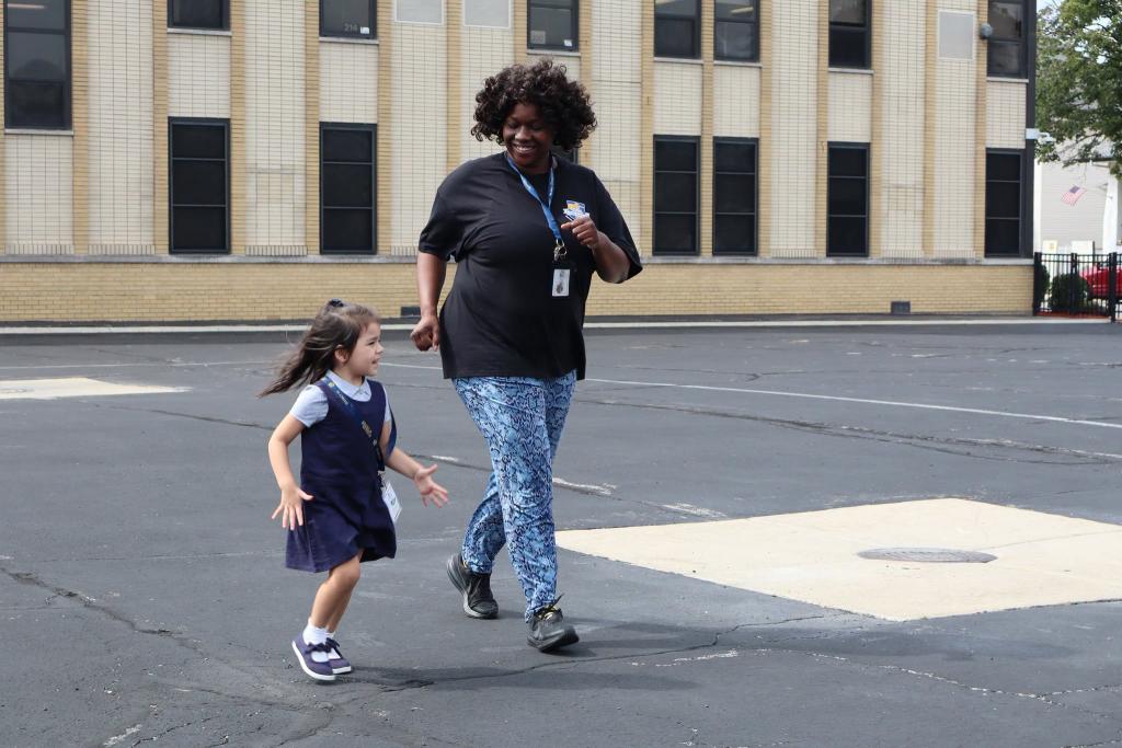 A woman and a young child walk together on a paved surface in front of a building.