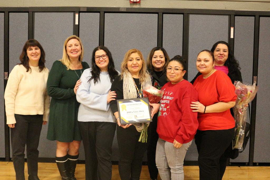 A group of women pose together, holding a certificate and flowers.