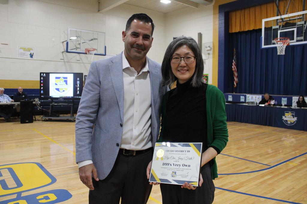Two people stand together in a gymnasium, one holding an award.