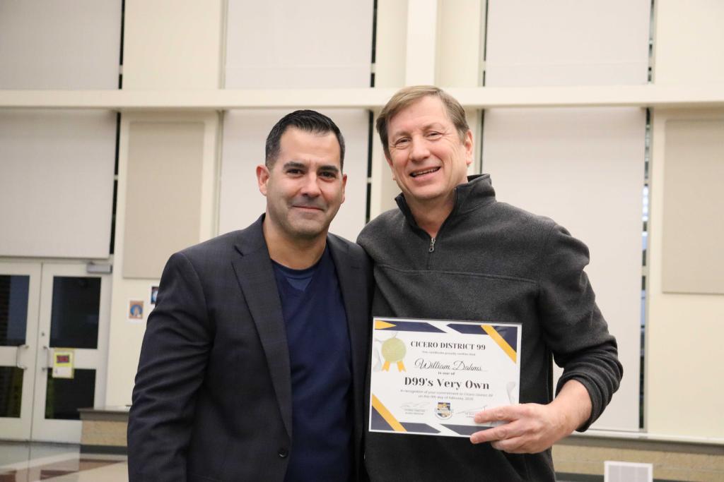 Two men smile, posing together, one holding a certificate.
