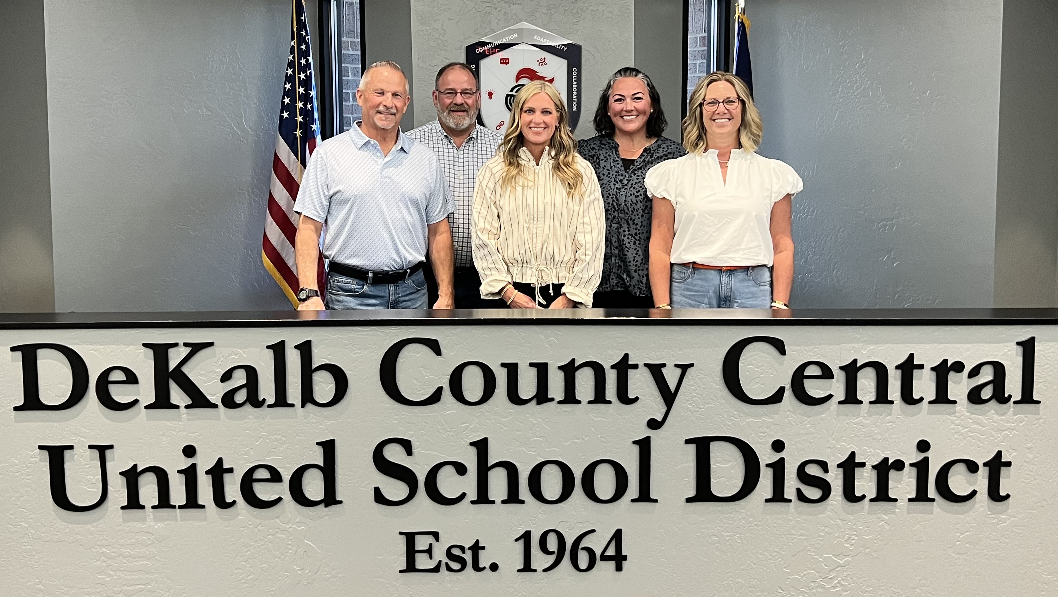 A group of six people stand behind a desk with the words 'DeKalb County Central United School District' on it.