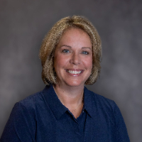 A woman with blonde hair smiles at the camera, wearing a blue shirt.