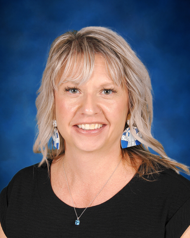 A woman with blonde hair smiles warmly against a blue backdrop.