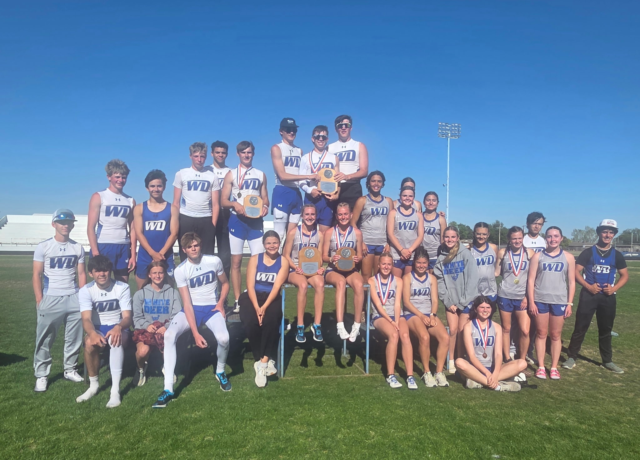 A large group of athletes poses for a team photo on a sunny field.