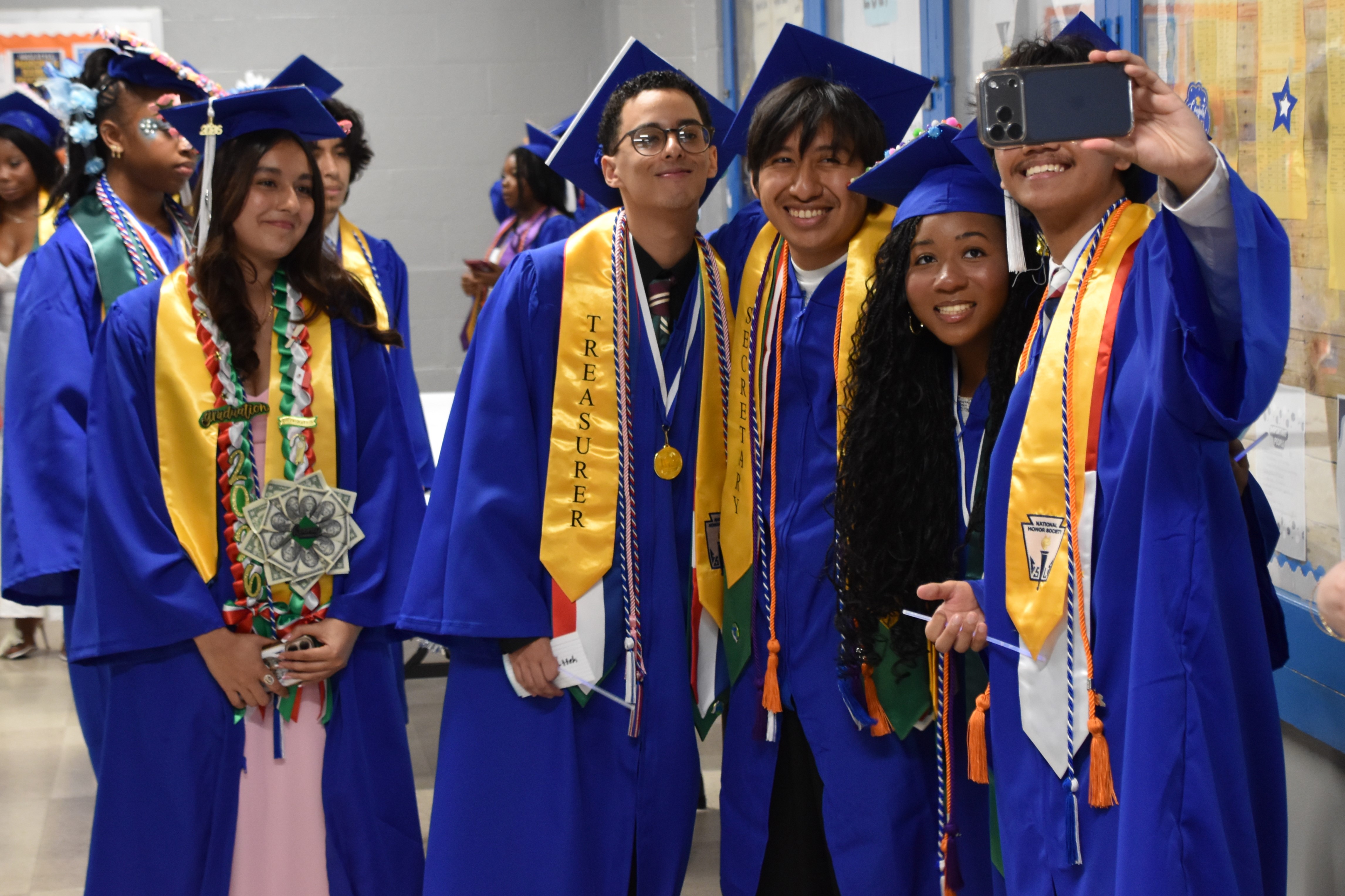 Graduates in blue gowns and caps pose for a selfie, celebrating their achievement.