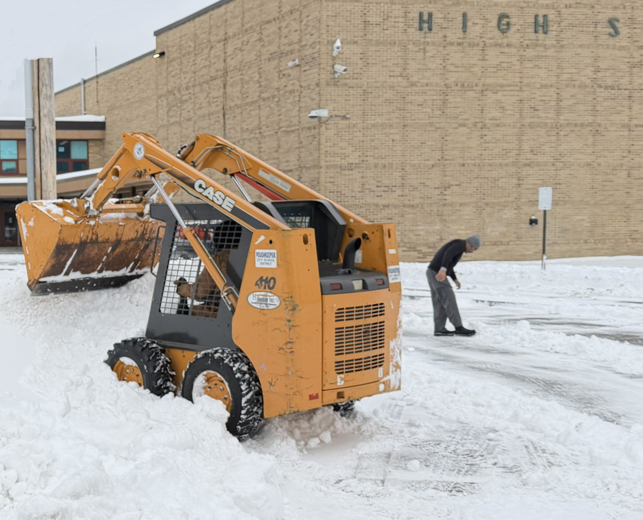A small construction vehicle clears snow from a parking area in front of a building.