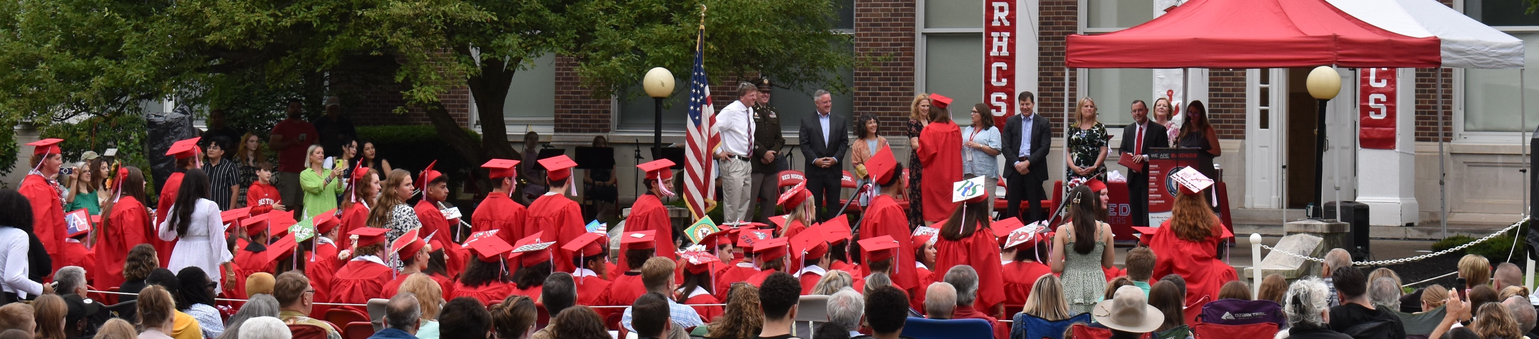 A large group of people wearing red shirts are gathered outdoors, some under a red tent.