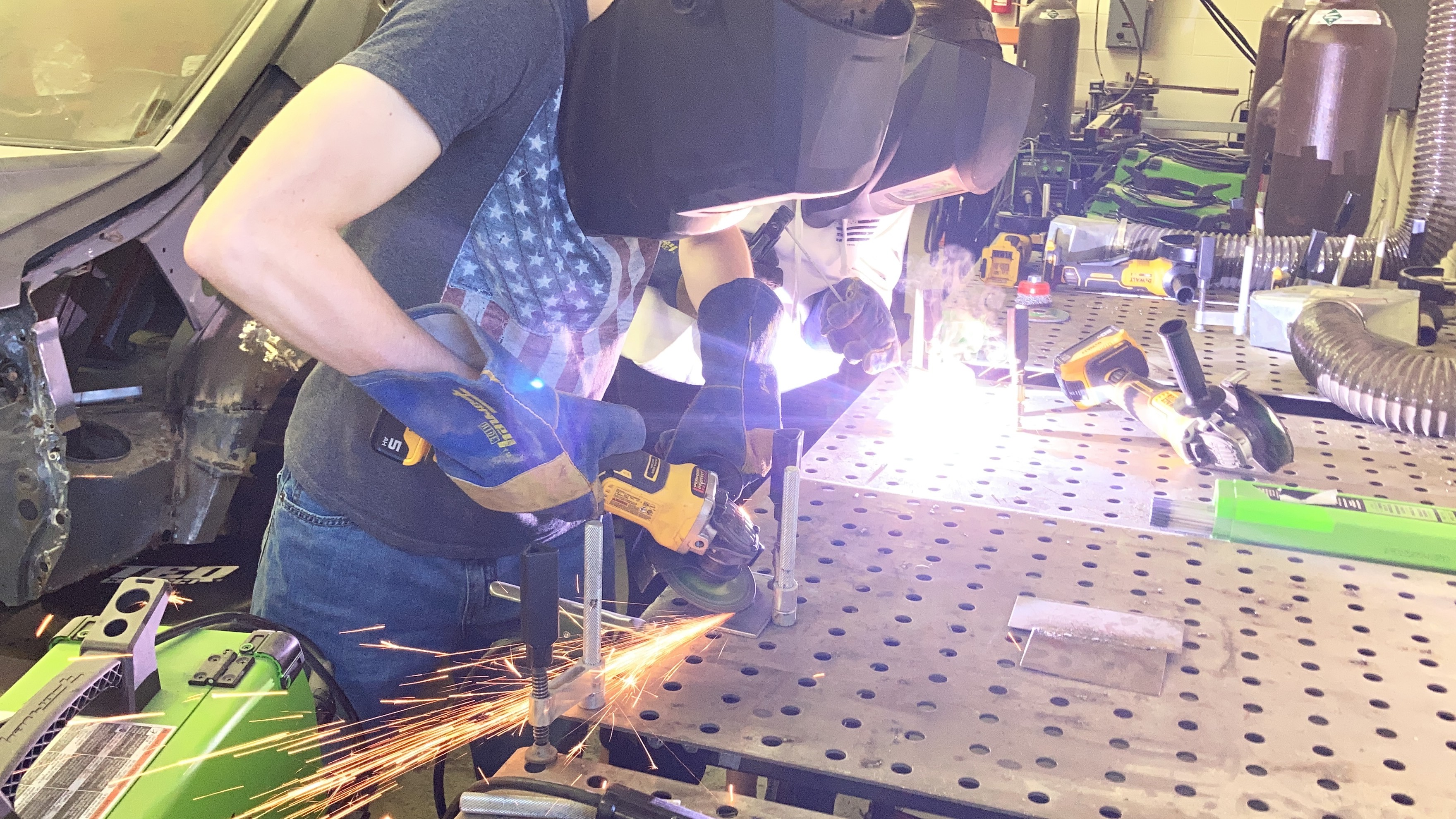 A person welds metal in a workshop, wearing a protective mask and gloves.
