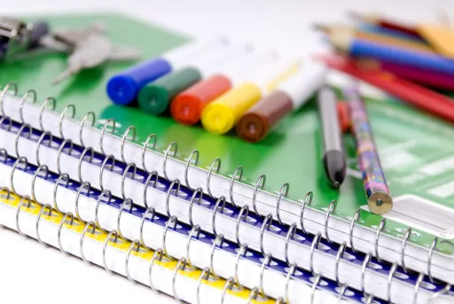A stack of spiral notebooks with colorful markers and pencils arranged on a green notebook.