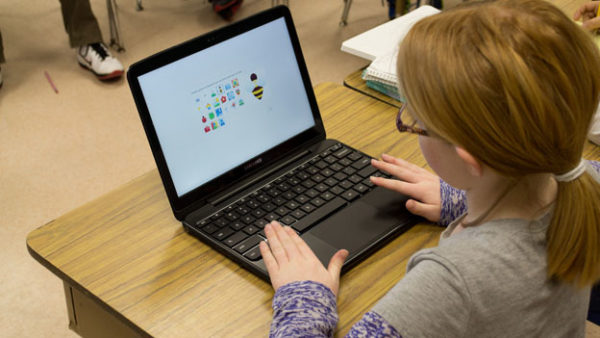 A young student types on a laptop in a classroom setting.