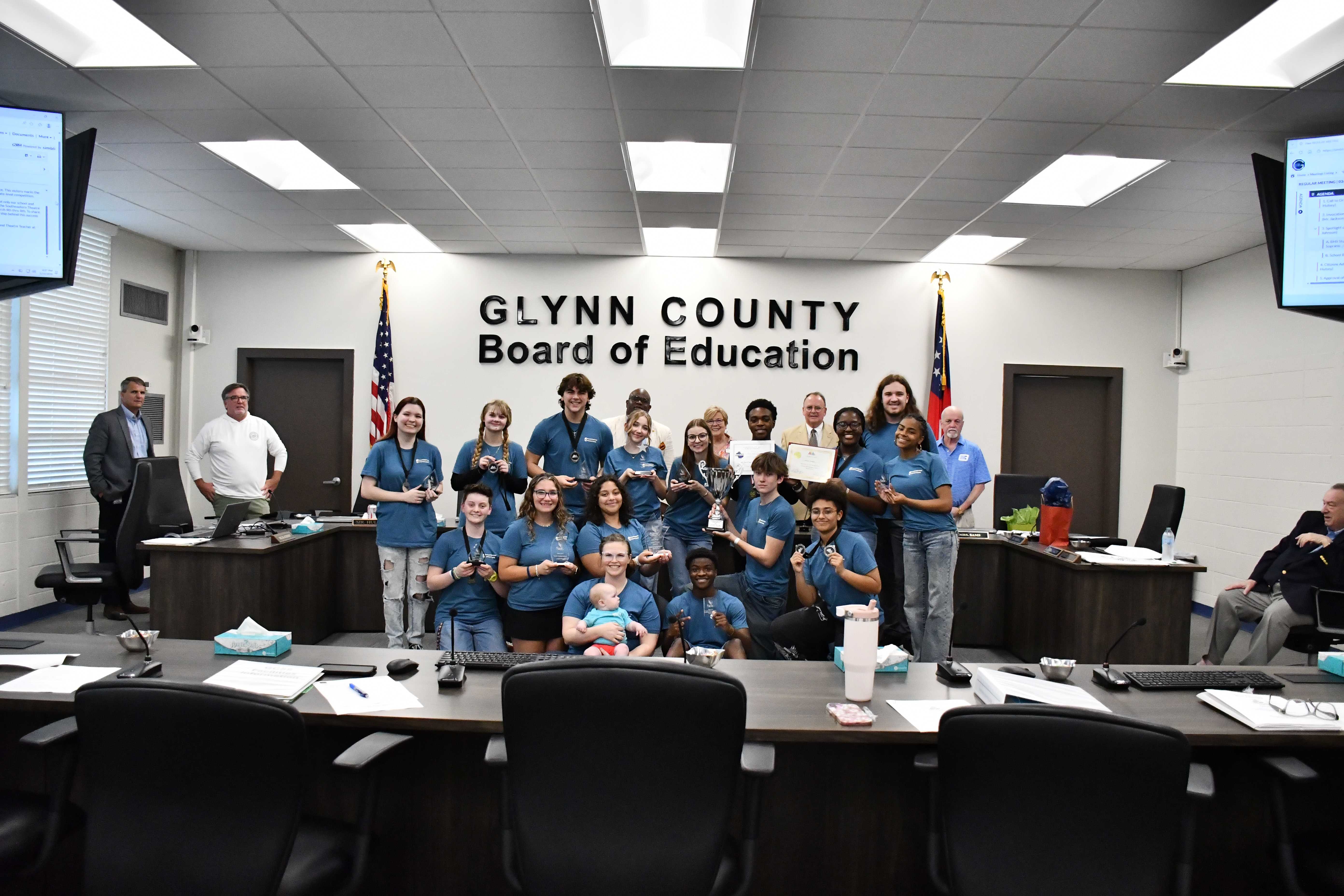 A group of people pose for a photo in a boardroom, holding trophies and awards.