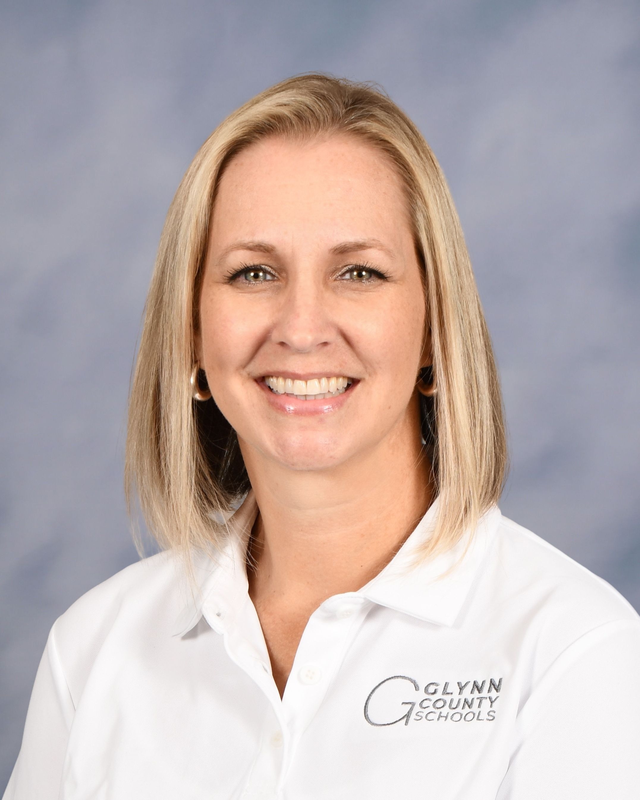 A woman with blonde hair smiles at the camera, wearing a white polo shirt with a logo.