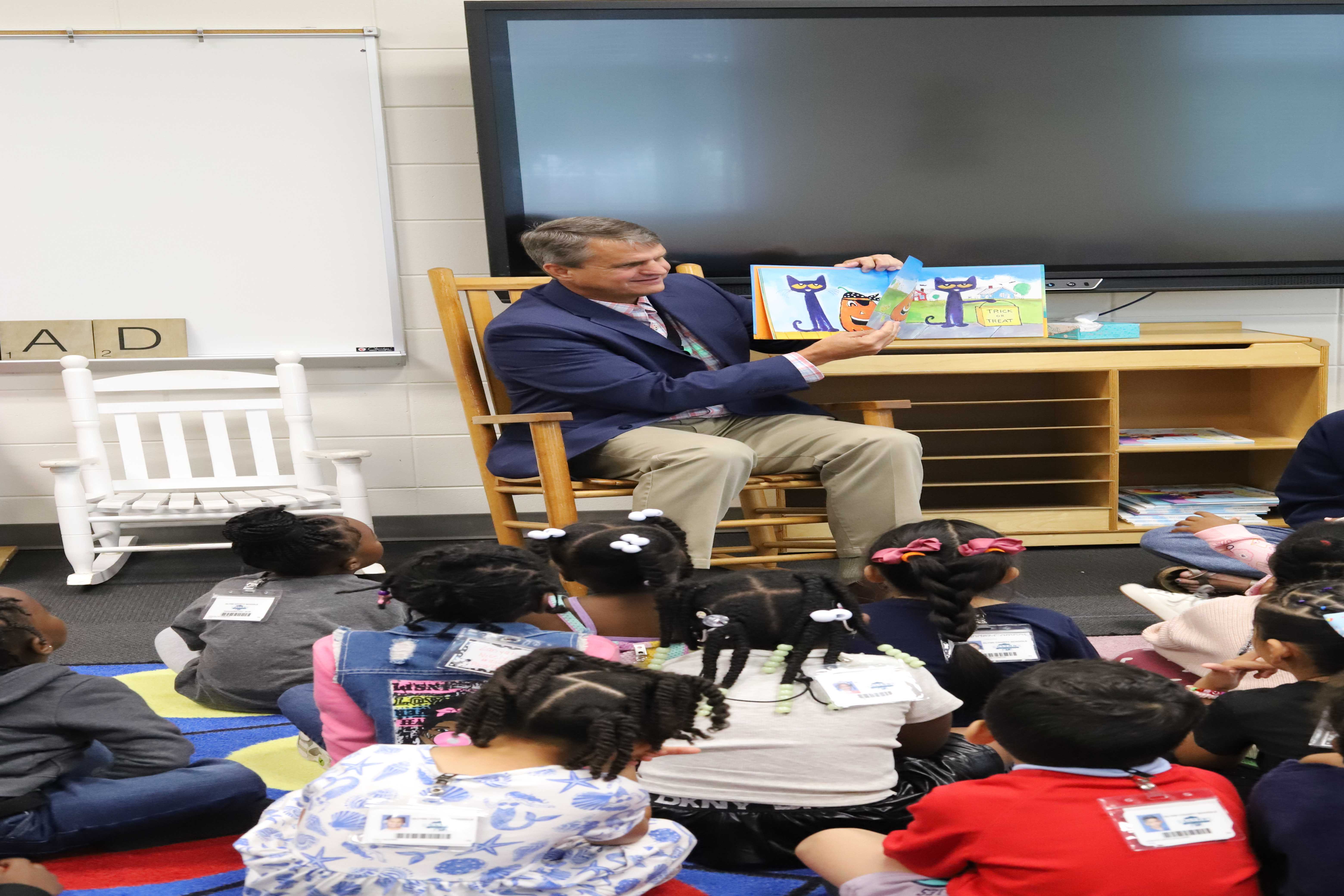Mike Blackerby reads a book to a group of children in a classroom setting.