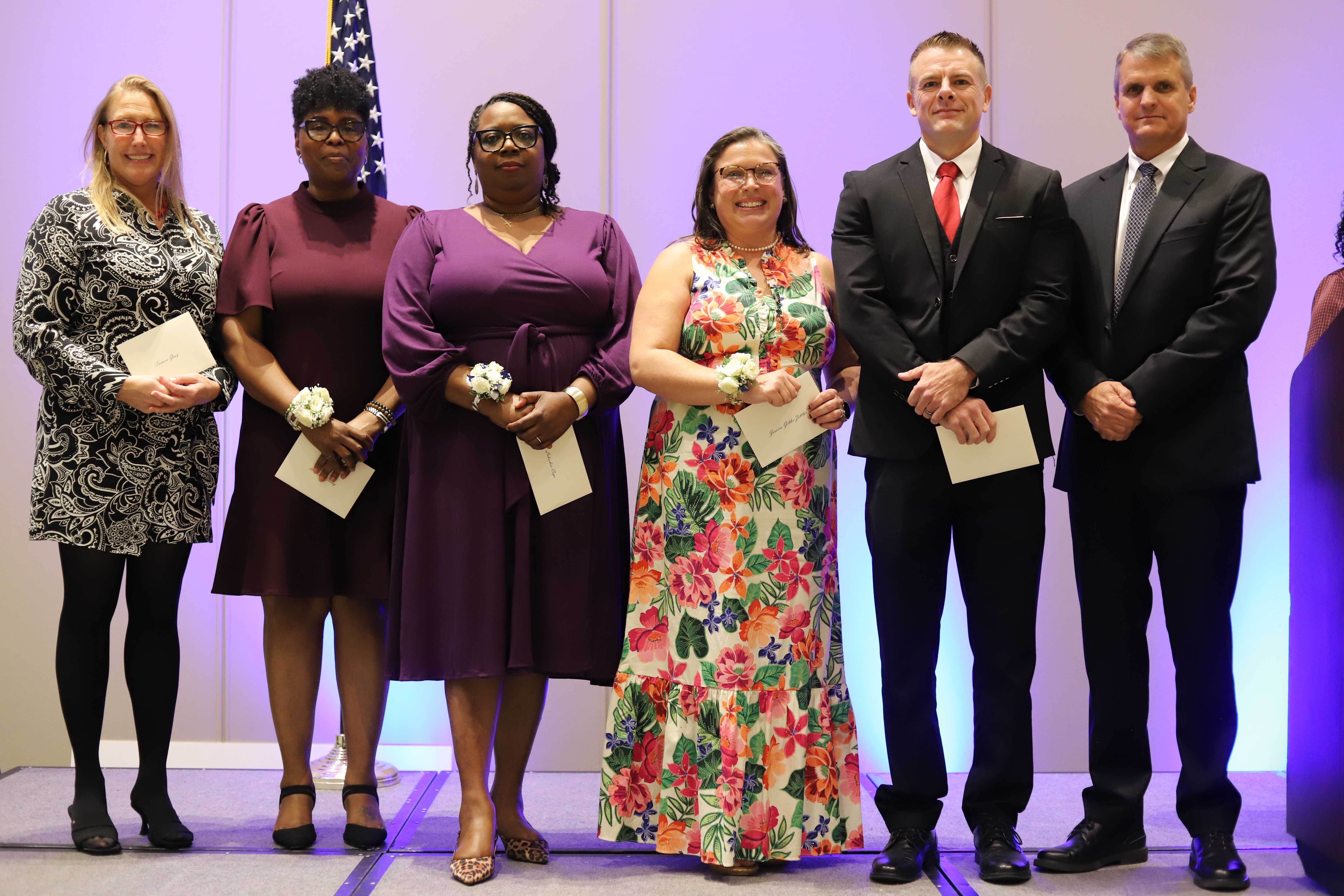 A group of people stand together, holding certificates, in front of an American flag.