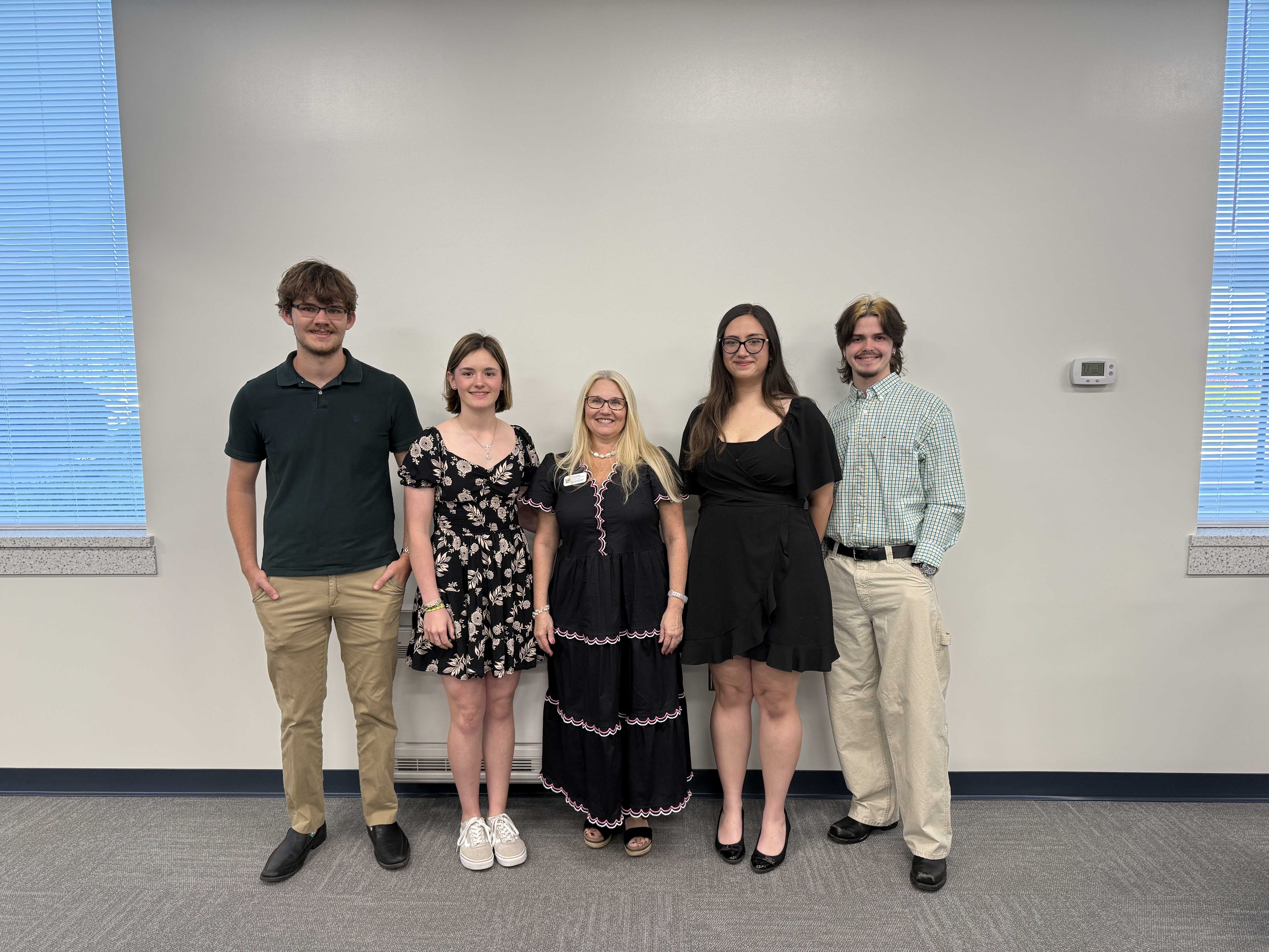 Five people stand together in front of a plain white wall, posing for a photo.