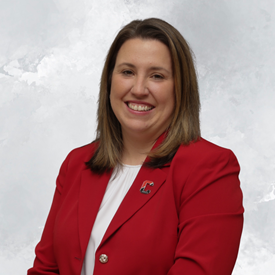 A woman with shoulder-length brown hair smiles, wearing a red blazer.
