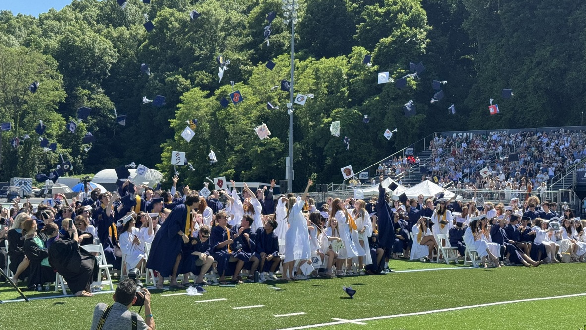 Graduates in caps and gowns throw their hats in the air during an outdoor ceremony.