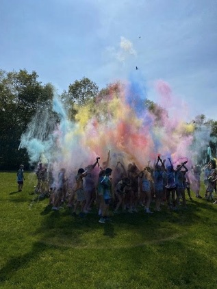 A group of people are joyfully throwing colorful powder into the air, creating a vibrant cloud.