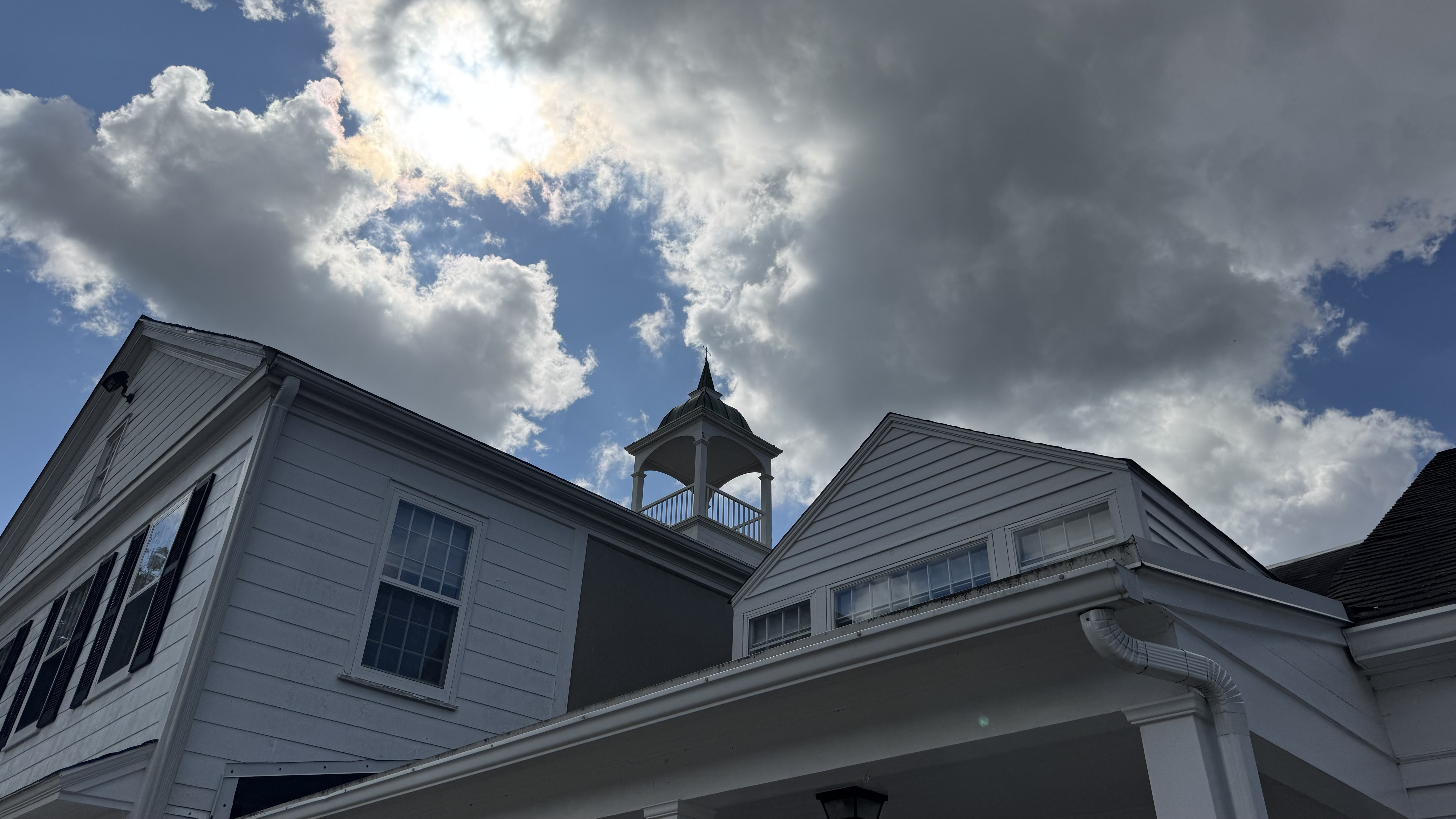 A white building with a cupola stands against a dramatic sky with clouds.