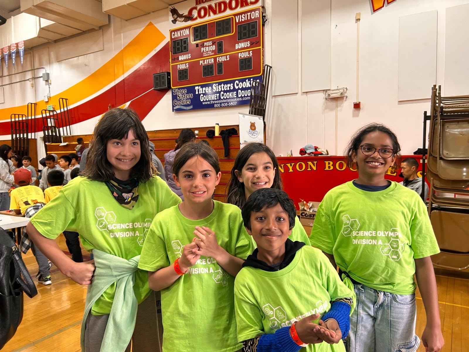 A group of five young people in bright green t-shirts pose for a photo indoors.