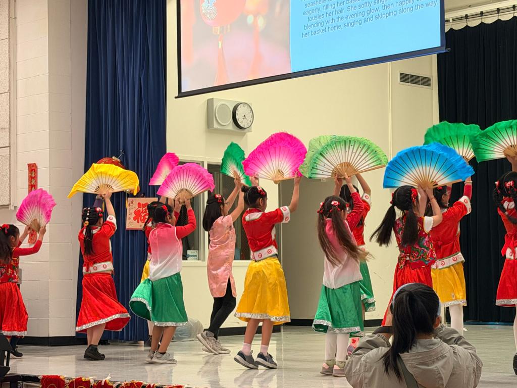 Children in colorful costumes perform a fan dance on a stage.