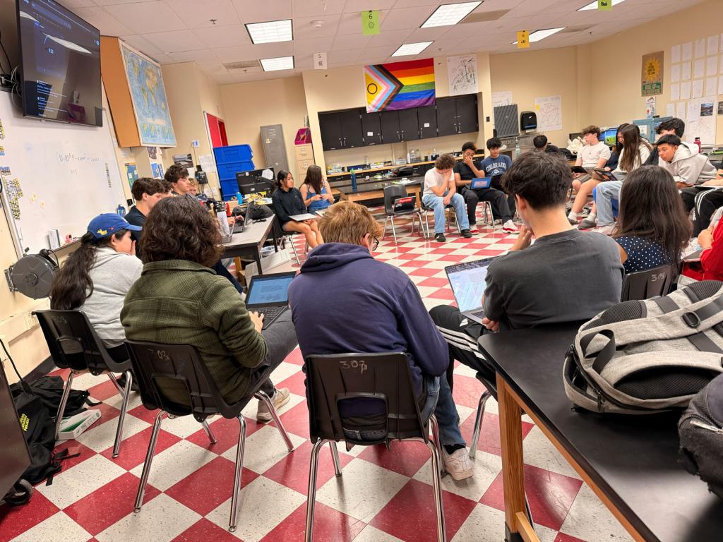 Students are seated at desks in a classroom, facing forward.