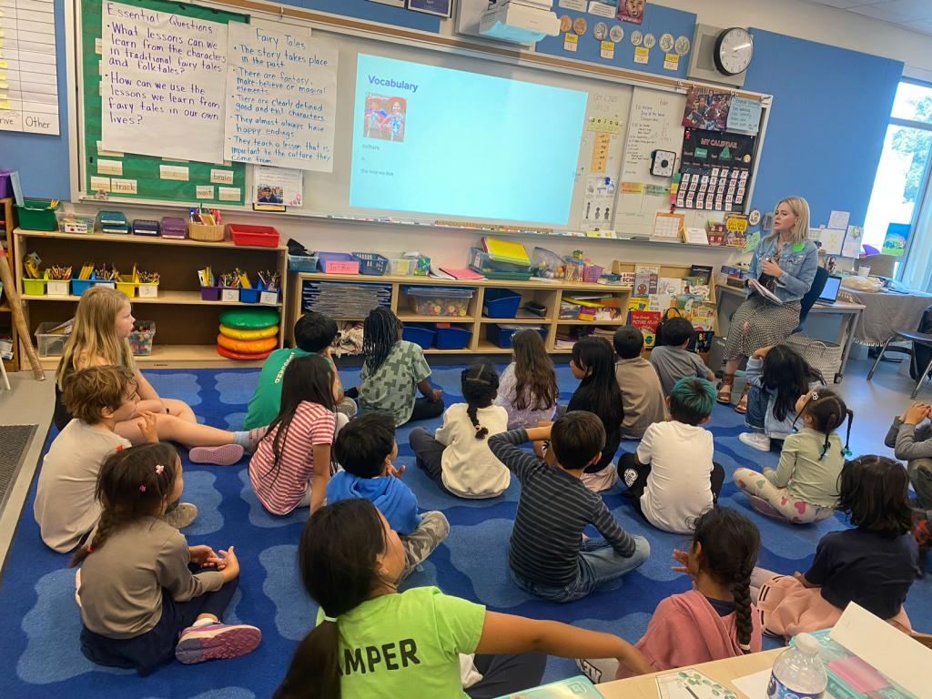 A teacher reads to a group of young students sitting on a blue rug in a classroom.