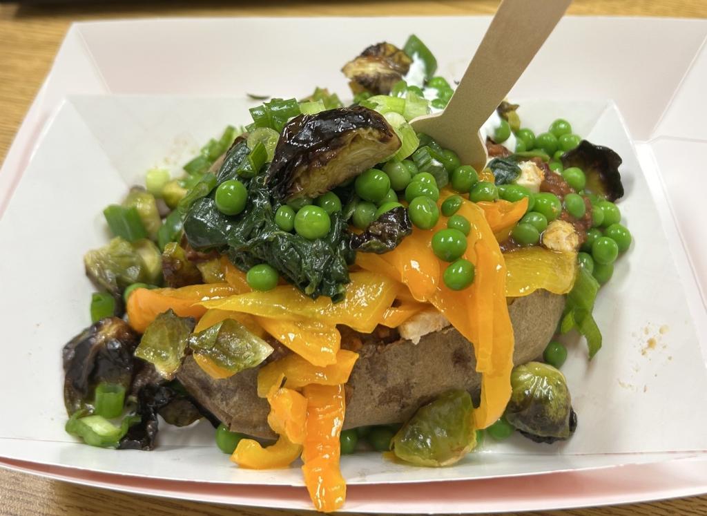 A baked potato topped with a colorful medley of peas, peppers, and greens.
