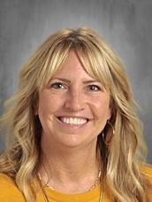 A smiling woman with blonde, wavy hair and bangs, wearing a yellow shirt, poses for a headshot.