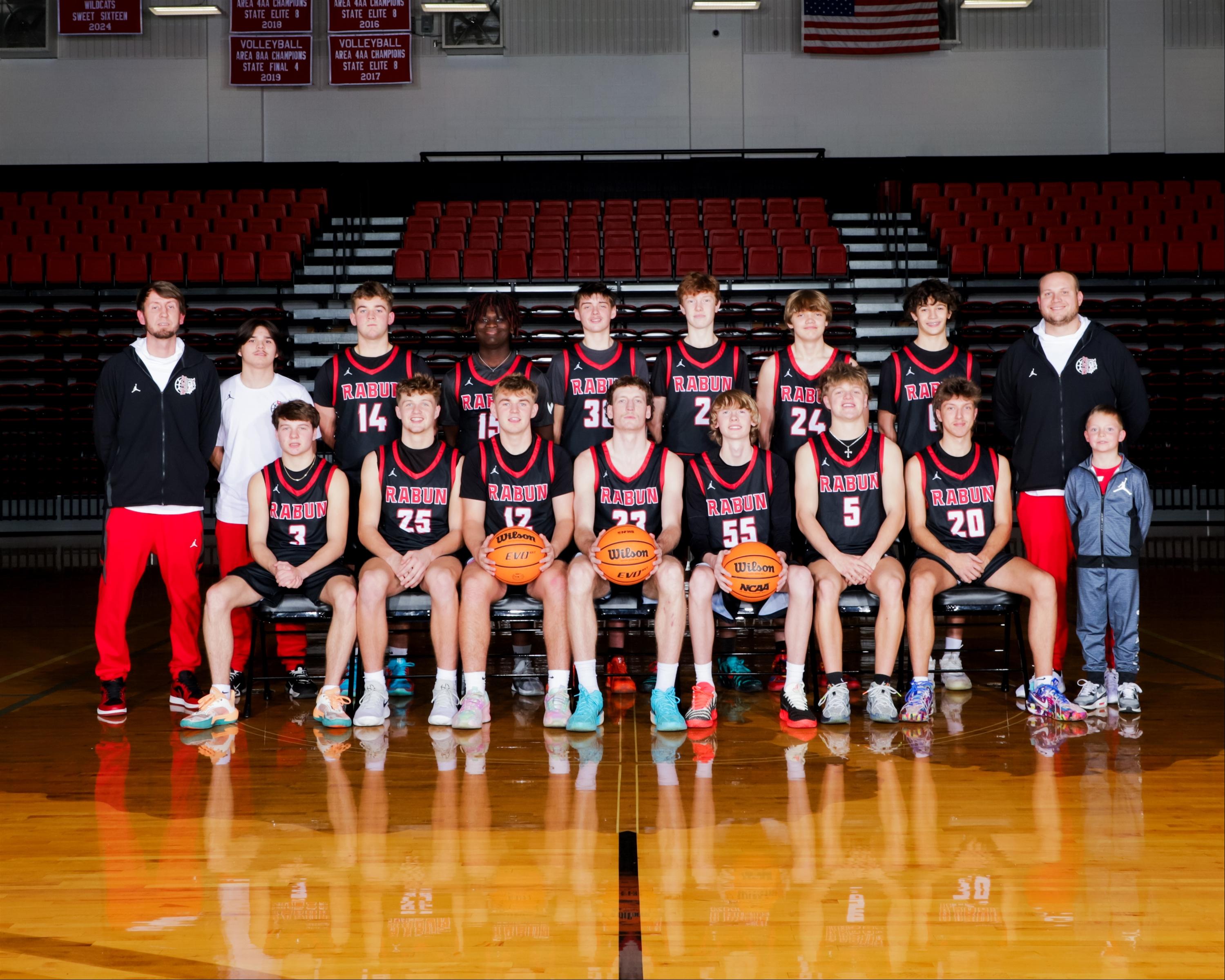 A basketball team poses for a group photo in a gymnasium.