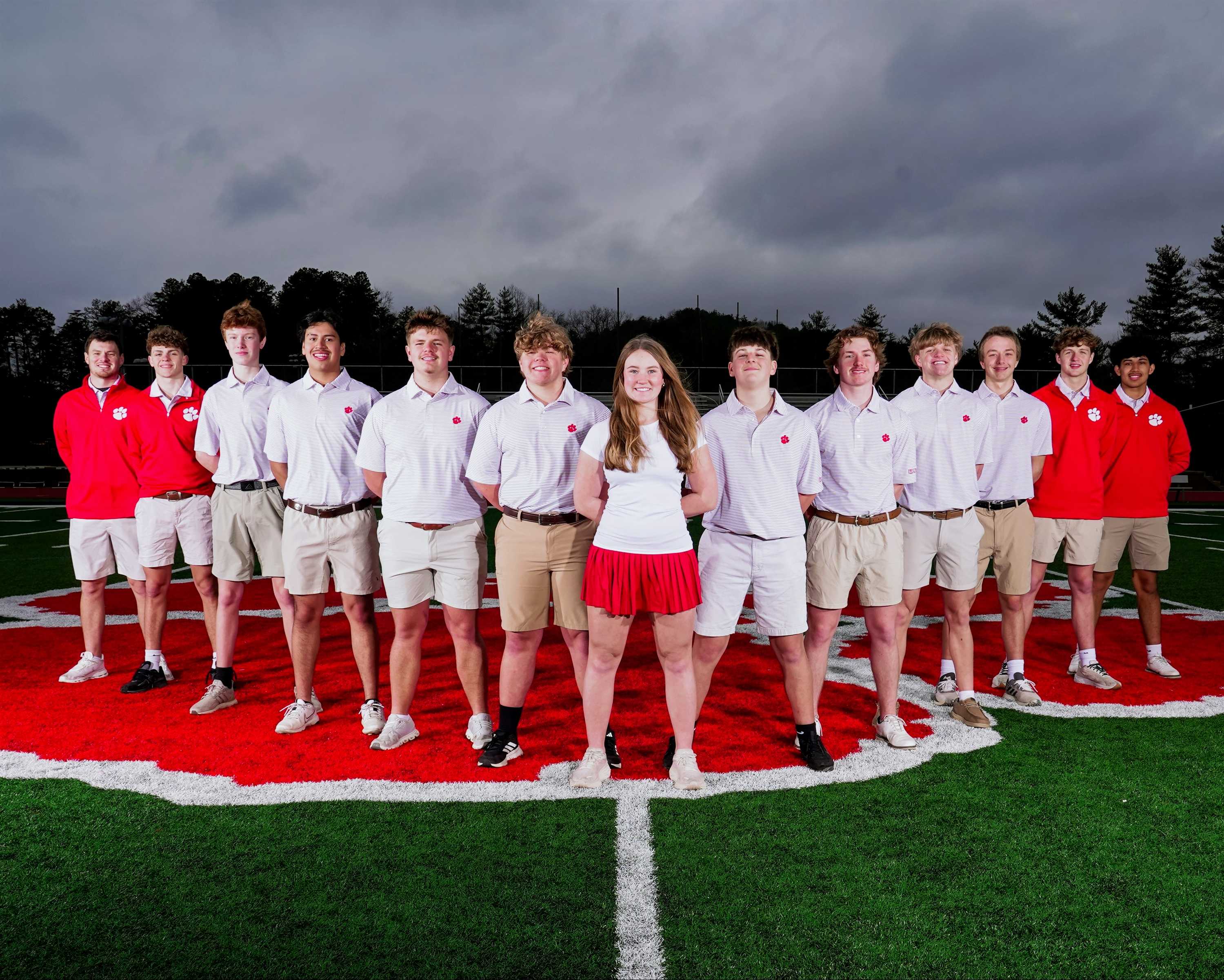 A team of young people poses on a red and green field, wearing white and red uniforms.