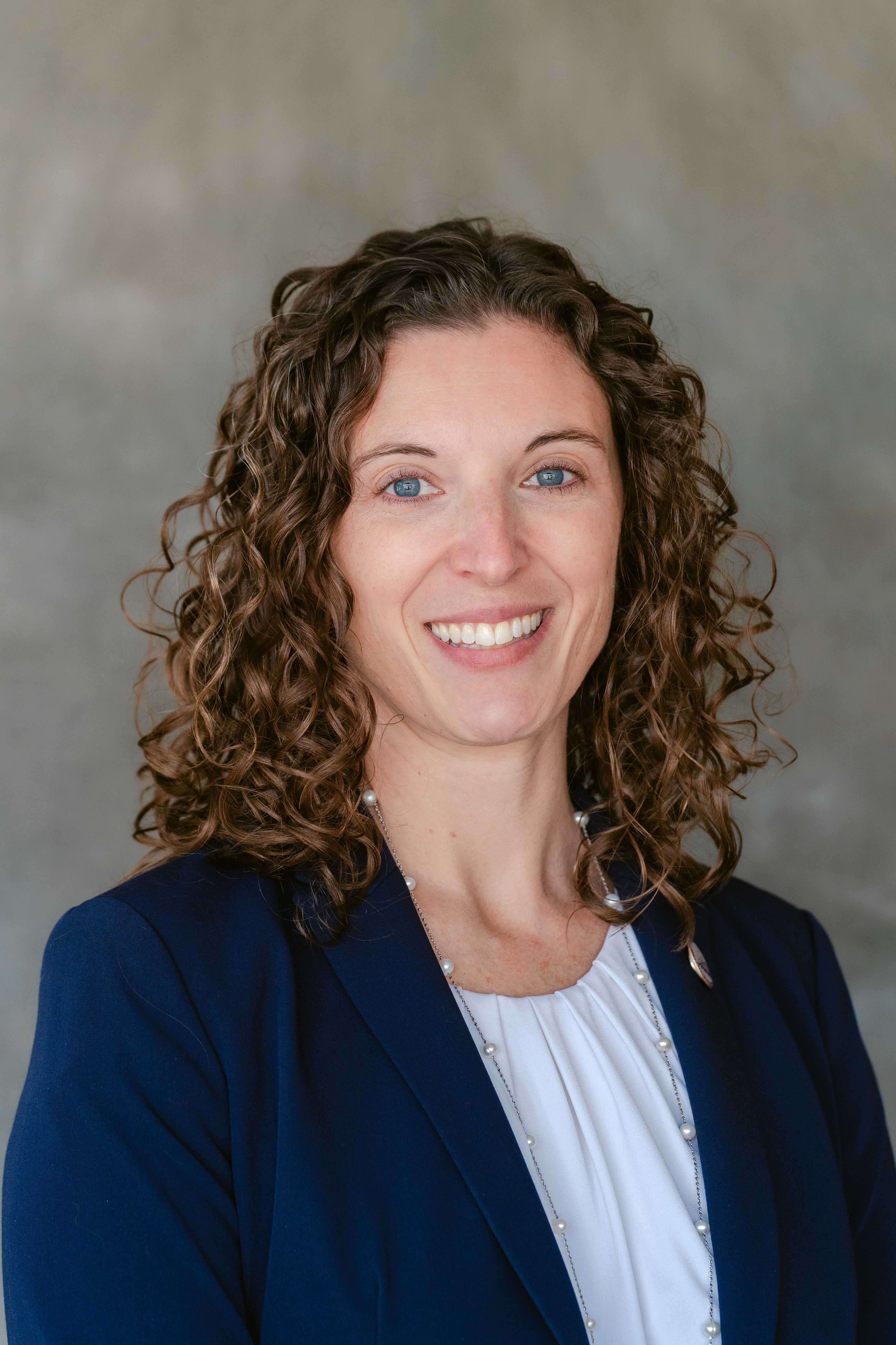 A woman with curly brown hair smiles at the camera.