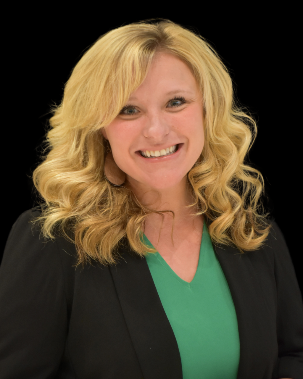 A woman with blonde hair smiles at the camera, wearing a blazer and green top.