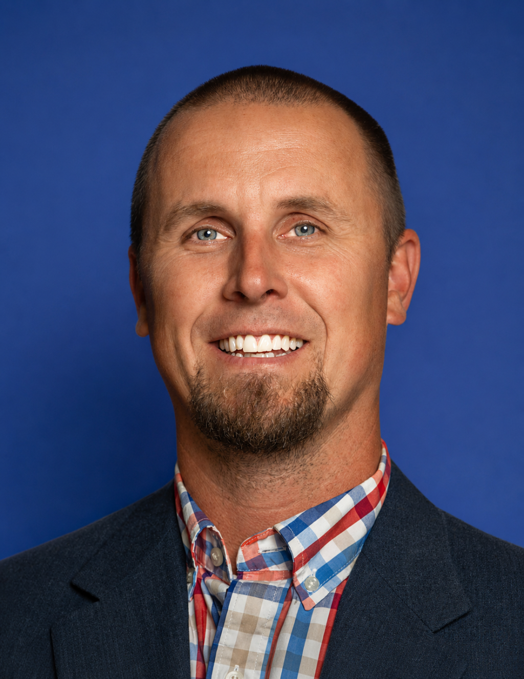 A man with a goatee and blue eyes smiles at the camera against a blue background.