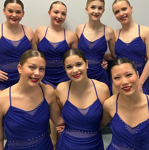 A group of young women in matching blue dresses smile for the camera.