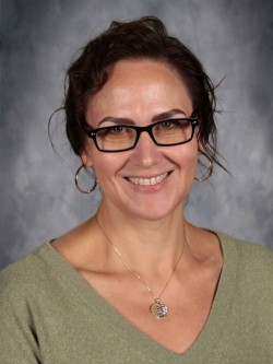 A woman with glasses smiles at the camera, wearing a green sweater.