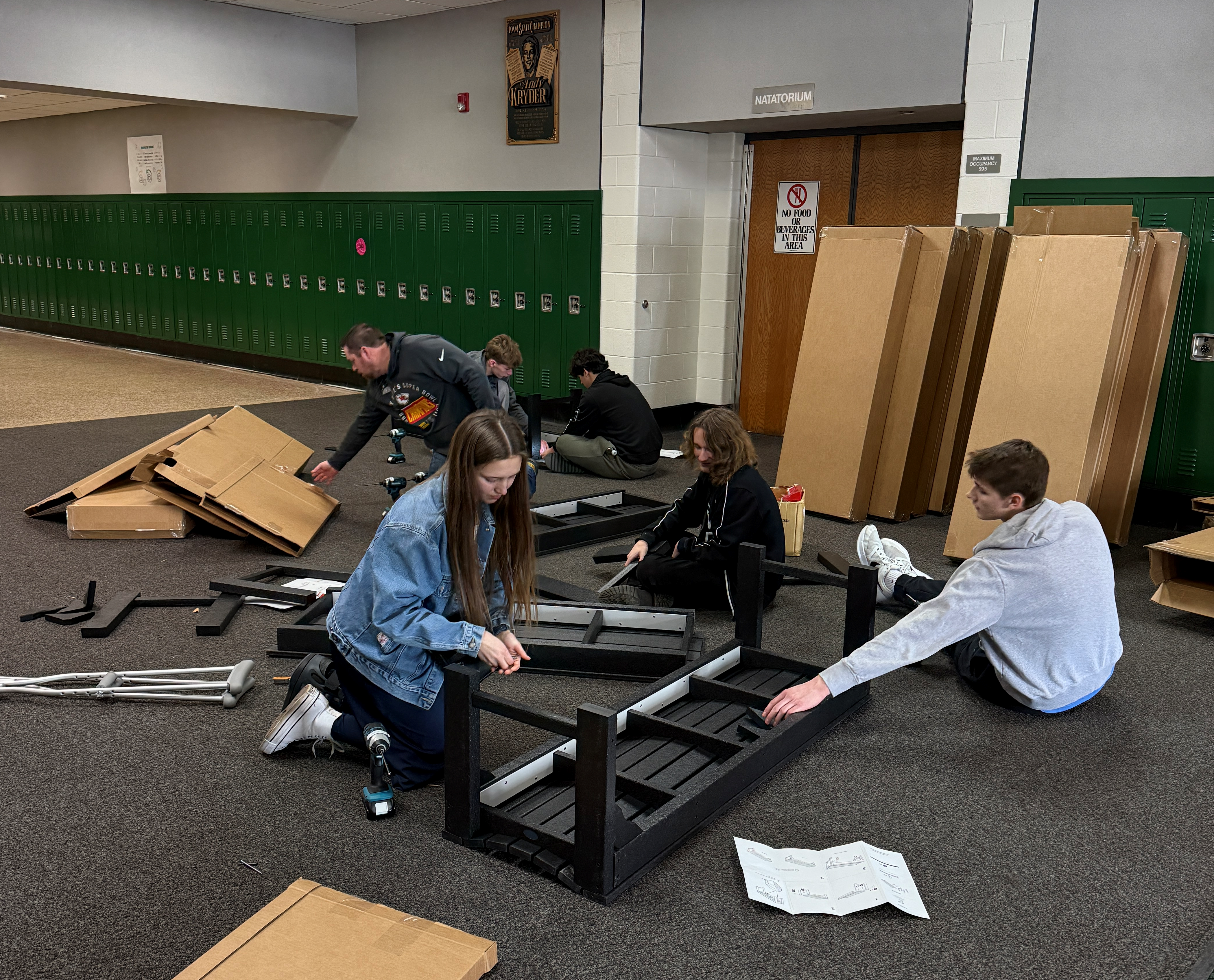 A group of people assemble furniture in a large room with lockers.